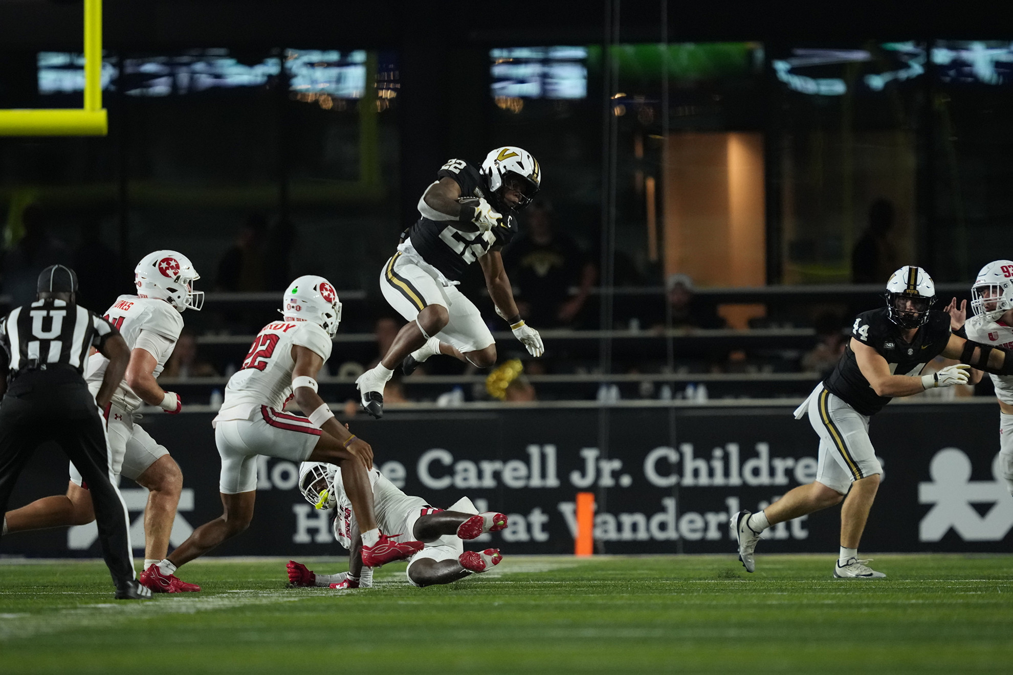 A football player in a black and white uniform leaps over opponents during a game at night.