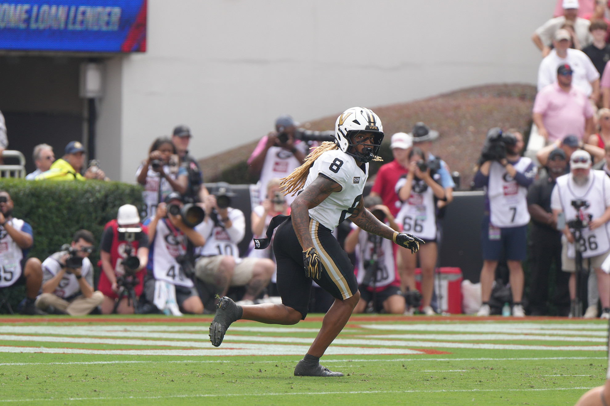 A football player in a white and black uniform with the number 8 runs across the field while photographers capture the moment.