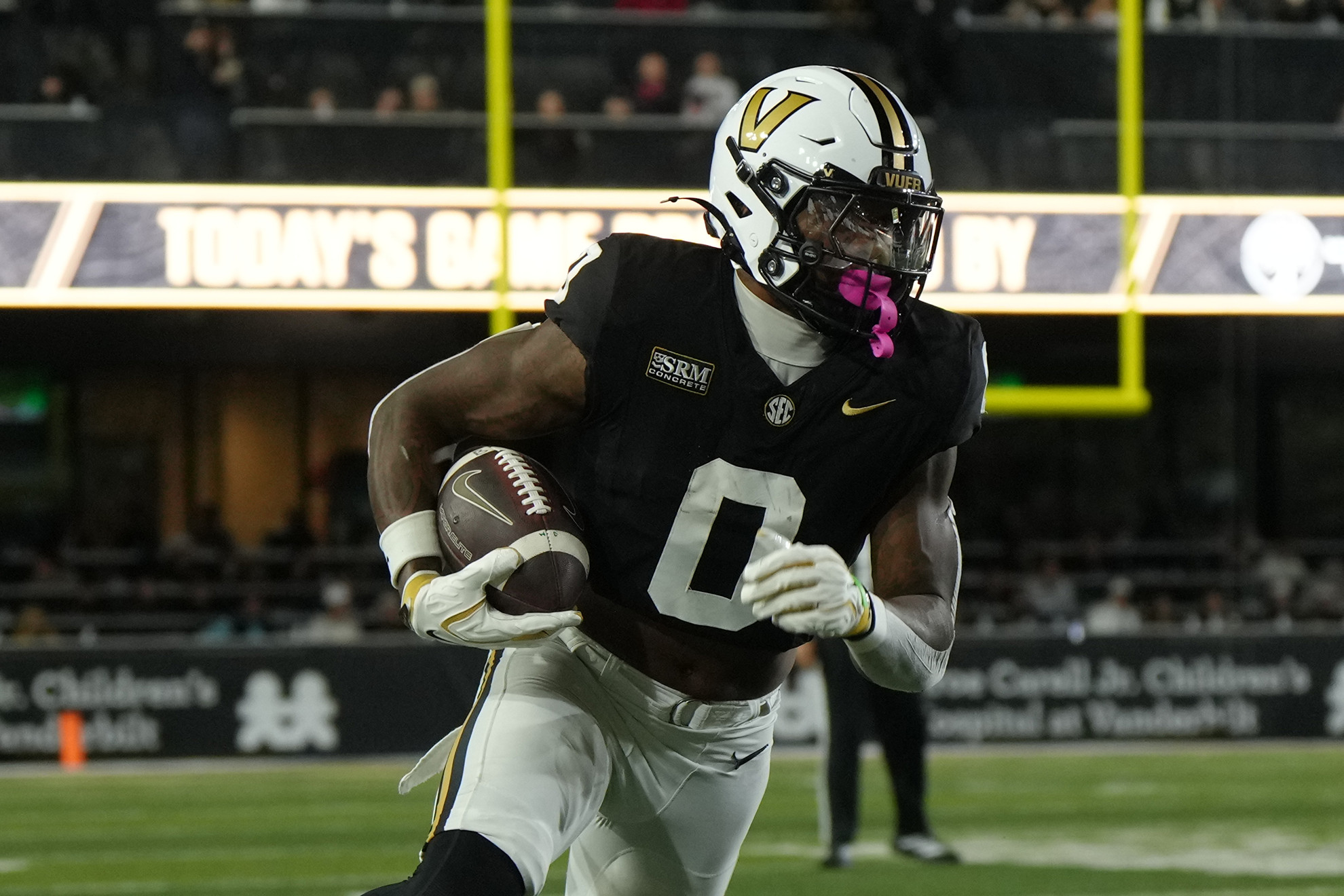 A football player in a black and white uniform with the number 0 runs with the ball during a game.